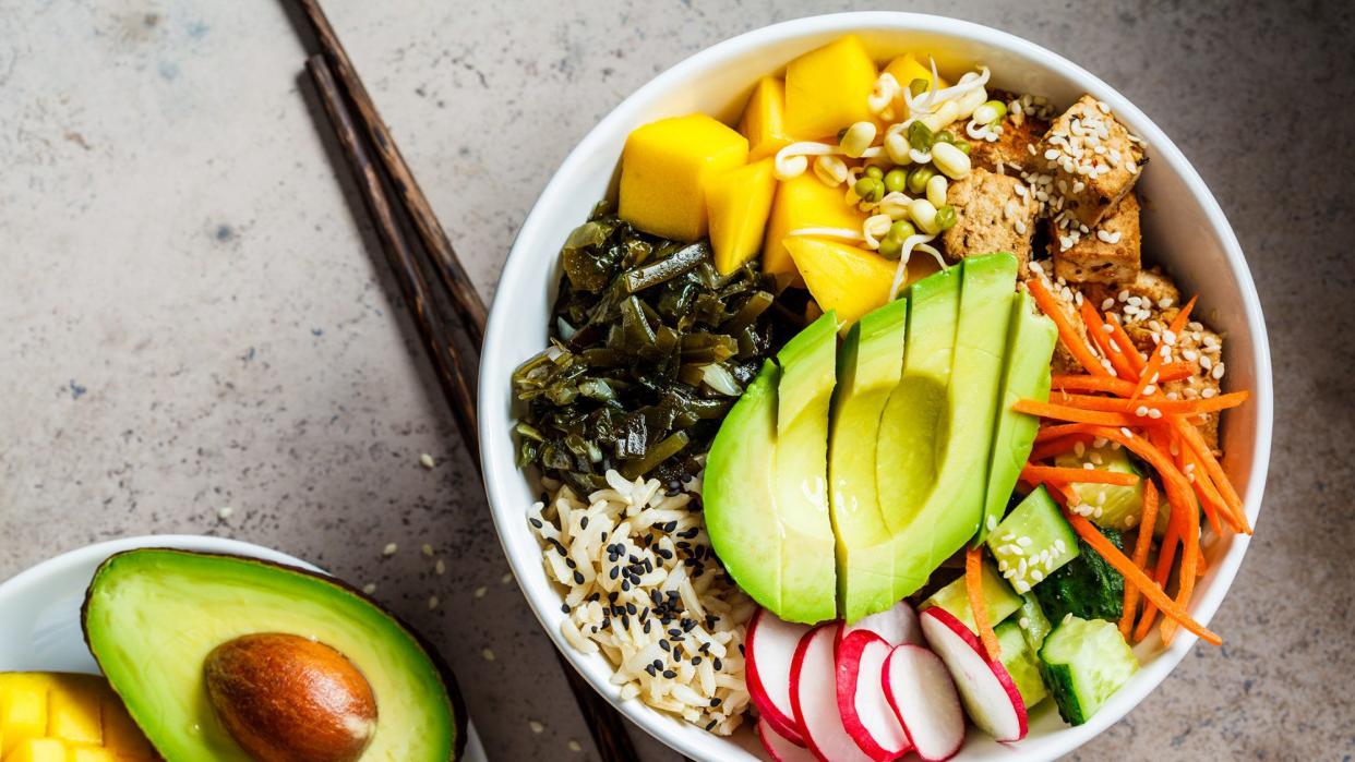 Vegan poke bowl with avocado, tofu, rice, seaweed, carrots and mango, top view. Vegan food concept.