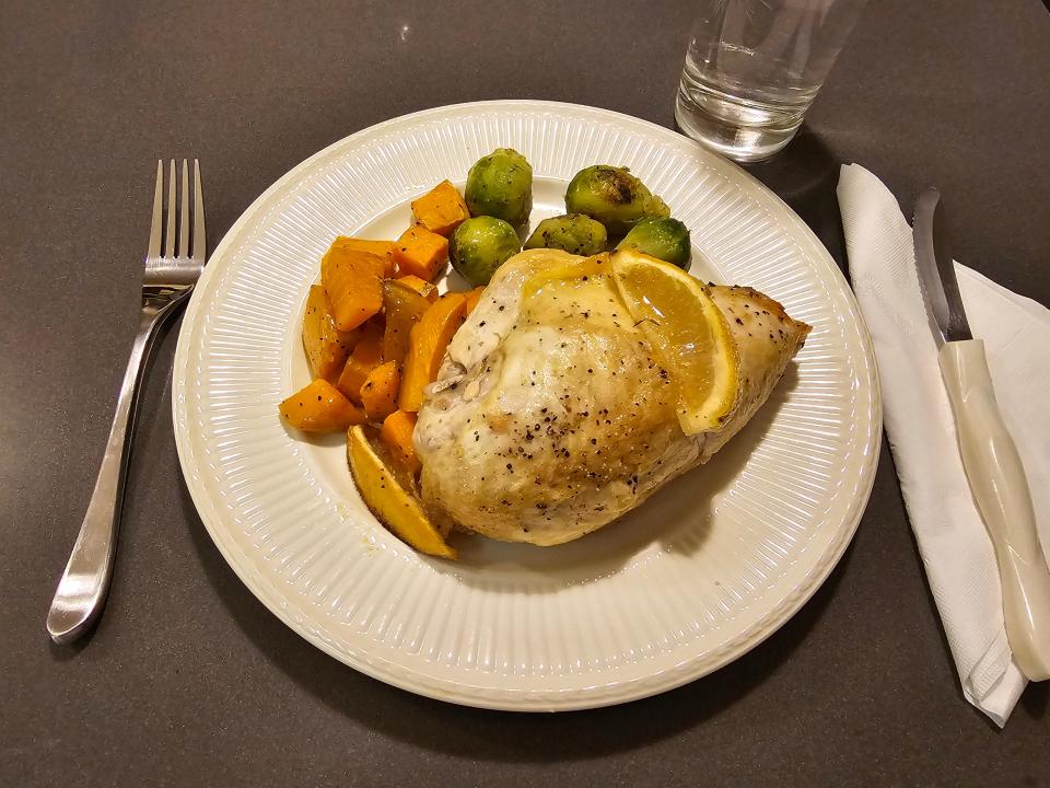 Lemno chicken on a plate with Brussels sprouts and sweet potato cubes and a lemon wedge