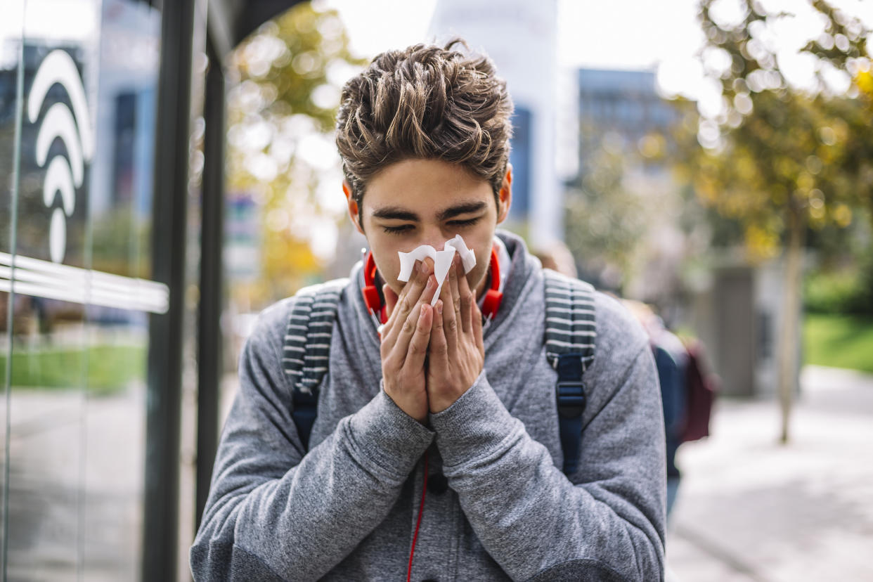 A person wearing a fall sweater sneezes into a tissue.