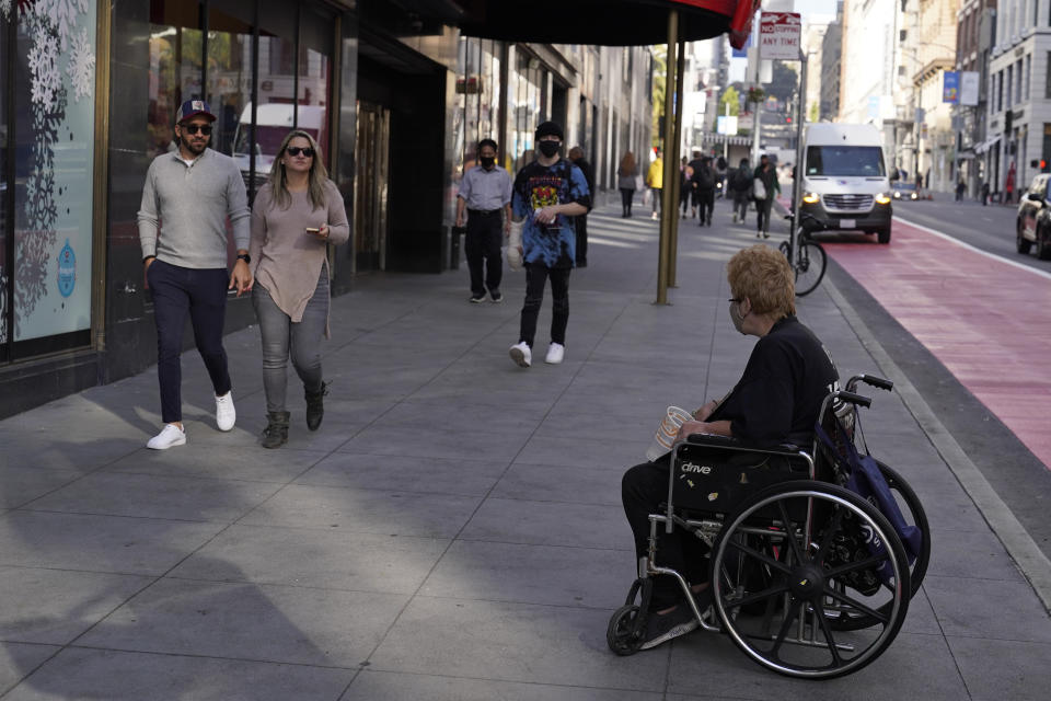 People pass by a woman in a wheelchair panhandling near Union Square in San Francisco, Thursday, Dec. 2, 2021. In San Francisco, homeless tents, open drug use, home break-ins and dirty streets have proliferated during the pandemic. The quality of life crimes and a laissez-faire approach by officials to brazen drug dealing have given residents a sense the city is in decline. (AP Photo/Eric Risberg)