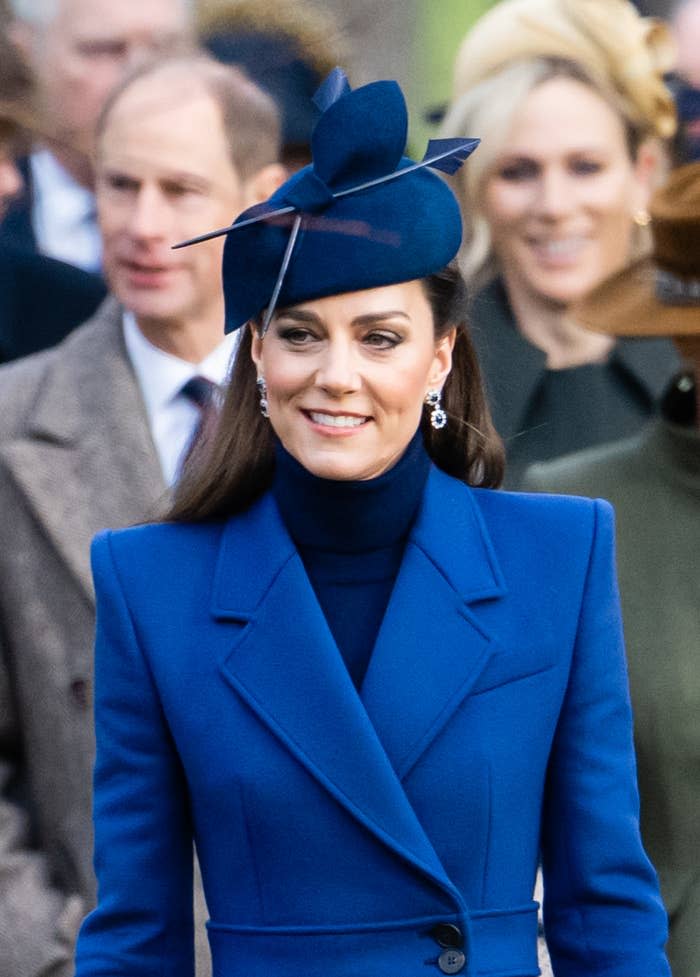 Woman in stylish blue hat and coat, adorned with earrings, at an outdoor event