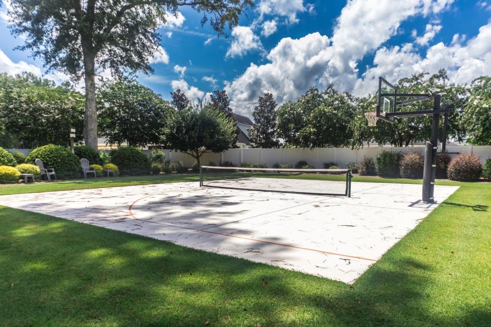 a large backyard with green grass and a basketball court that has been made into a home pickleball court