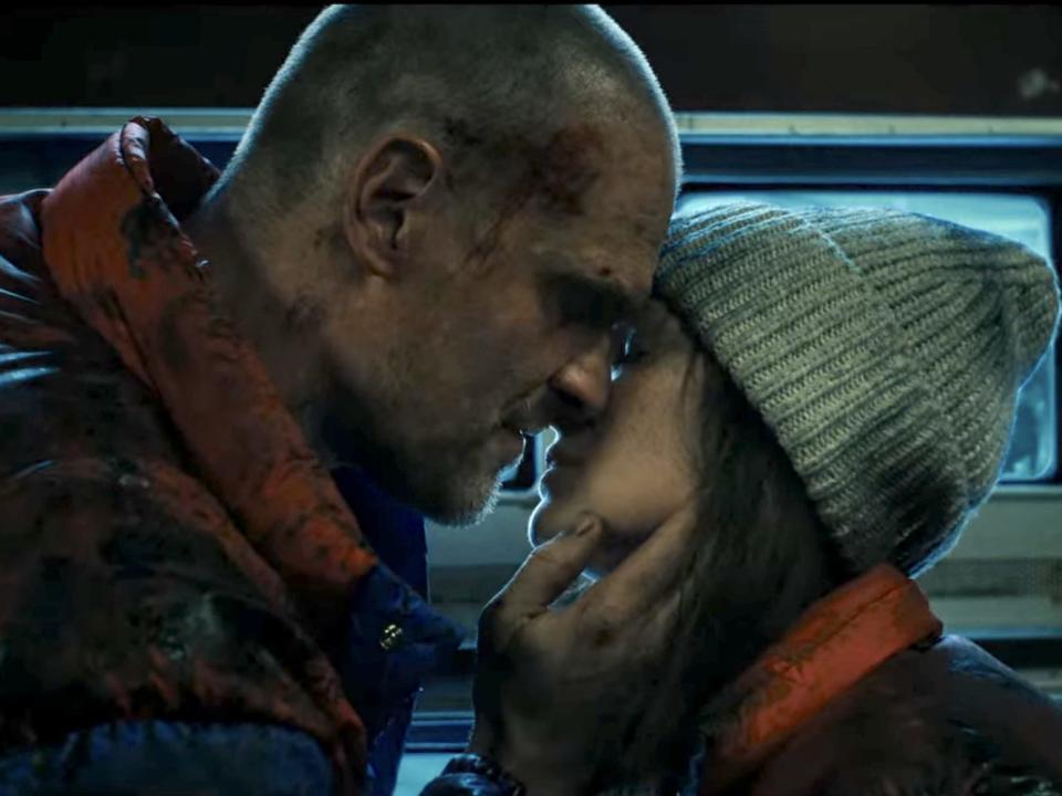 A man and woman, both covered in dirt and blood, kiss gently.