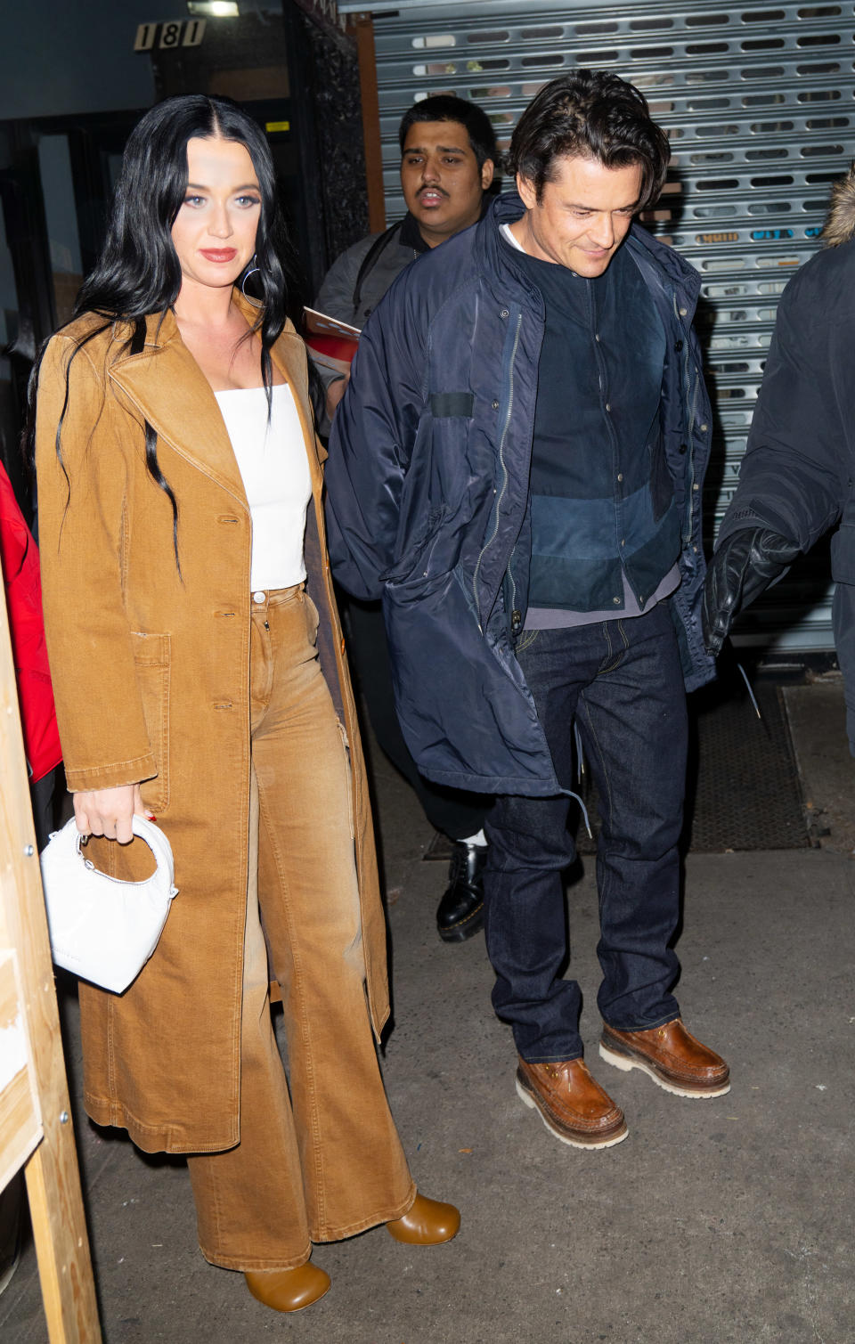 Katy Perry wears a long coat over a top and flared trousers as she walks with Orlando Bloom who's wearing a casual jacket and jeans