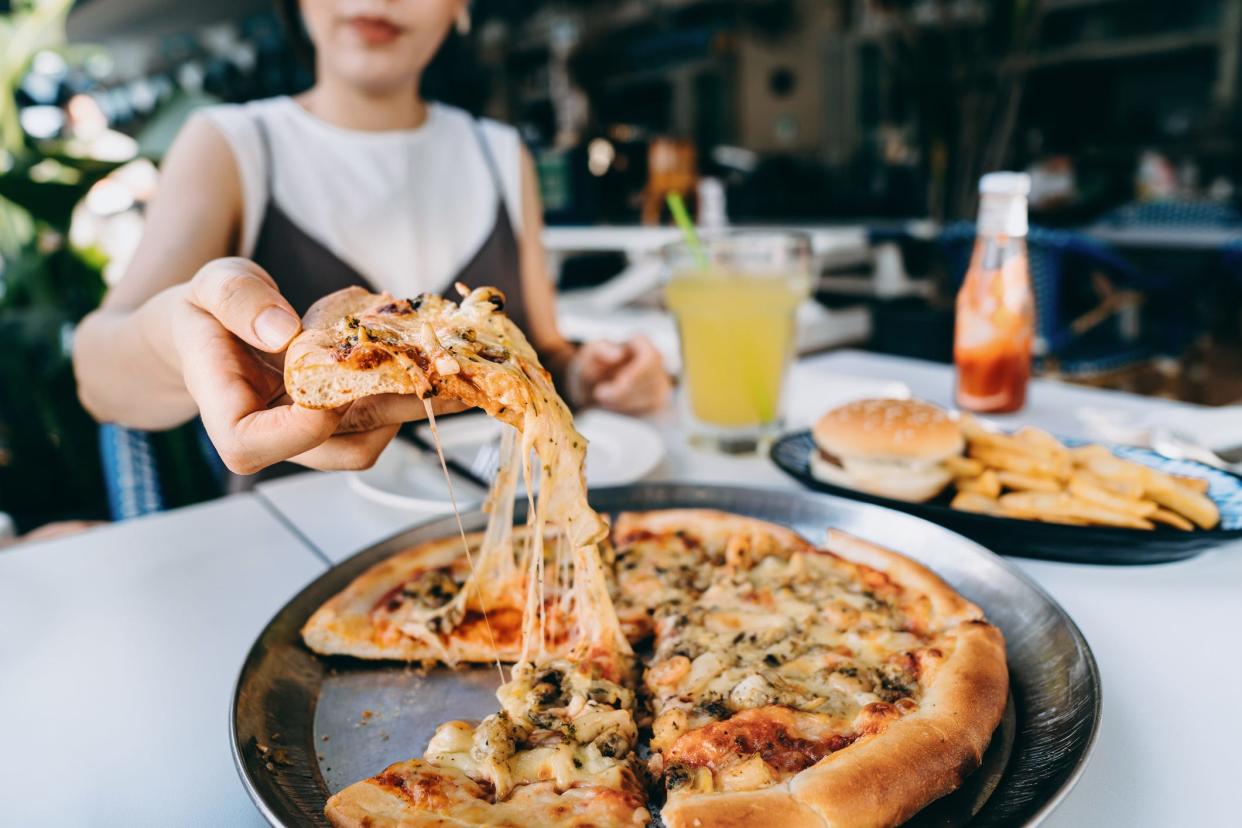 A woman sitting outside at a restaurant grabbing a piece of cheesy pizza.