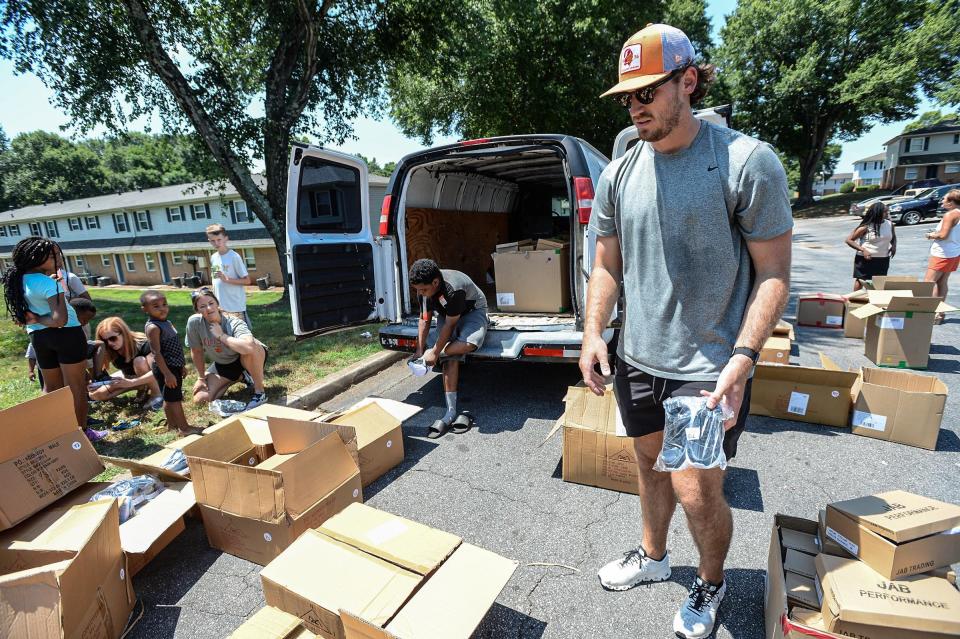 Bradley Pinion, left, of Salem, a kicker for the NFL Tampa Bay Bucs in 2021, and former Clemson Tiger, gives away shoes  400 boxes of shoes to people, with help from Anderson Interfaith Ministries and the Joy Comes Ministry of Powdersville, at Belton Woods Apartments in Anderson.