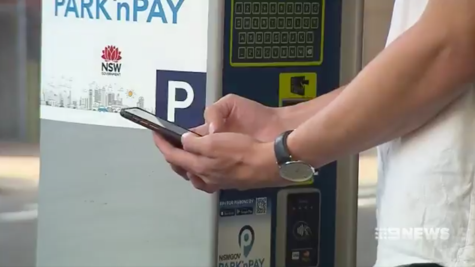 A man uses a phone next to a parking meter in Sydney.