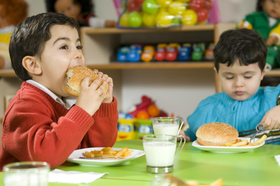 Two boys eating hamburgers with fries and milk. (Photo via Getty Images)