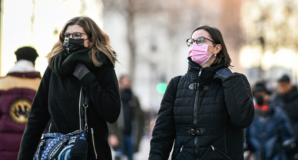 Two women walking around outside in jackets with cloth masks on.