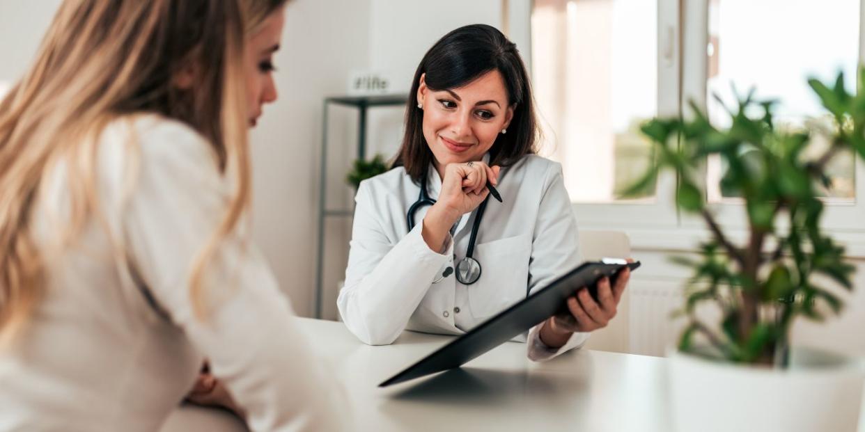 a woman in a white coat holding a clipboard and looking at a woman - anti-mullerian hormone test