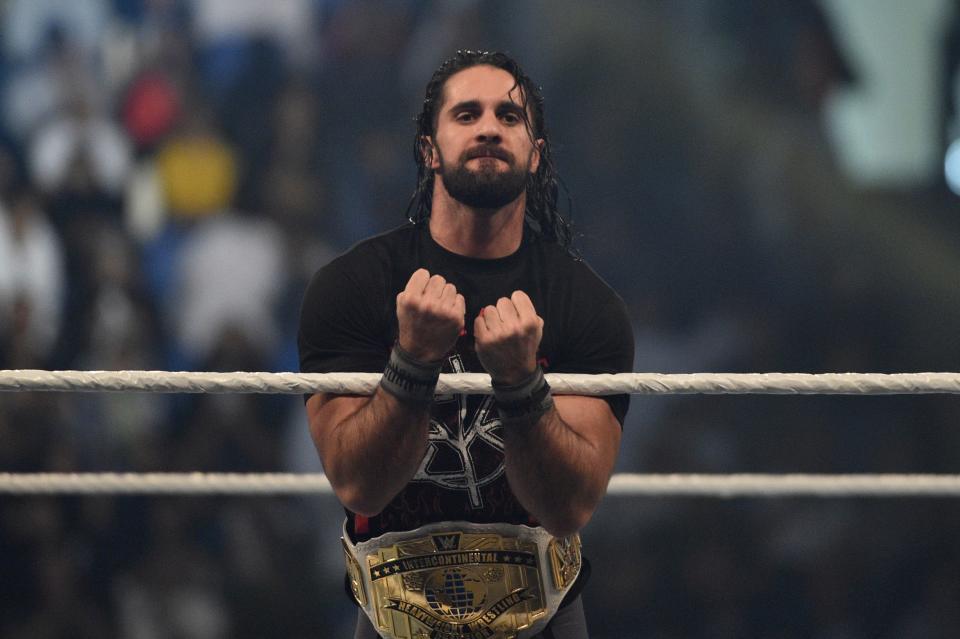 Seth Rollins stands in ring with belt.