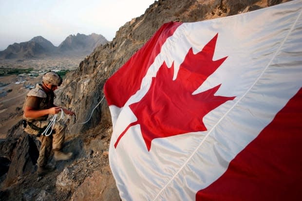 Canadian soldier Jeff Wright marks Canada Day by hanging the flag on a mountainside above the forward operating base of Ma'sum Ghar on July 1, 2007. (Finbarr O'Reilly/Reuters - image credit)