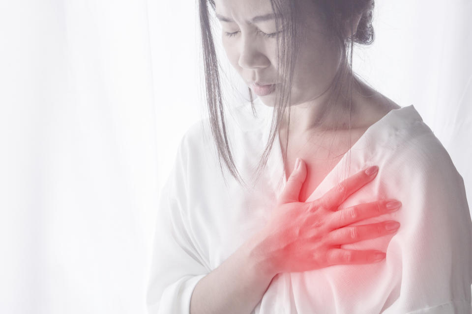 Asian woman standing against window with hand touching her chest in morning having heart attack