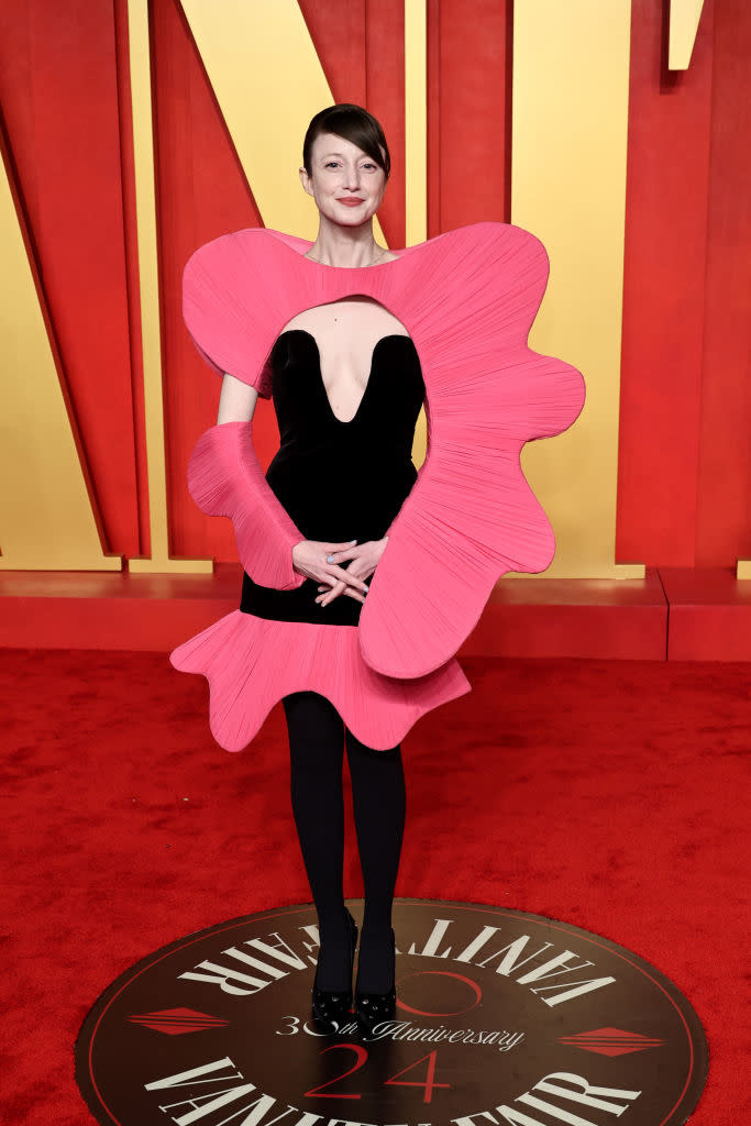 A person on the red carpet wearing a large pink flower-shaped outfit with a black center