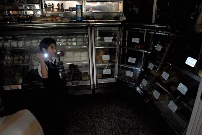 A boy uses a flshlight during a power cut at a bakery in the border state of San Cristobal on April 25, 2016