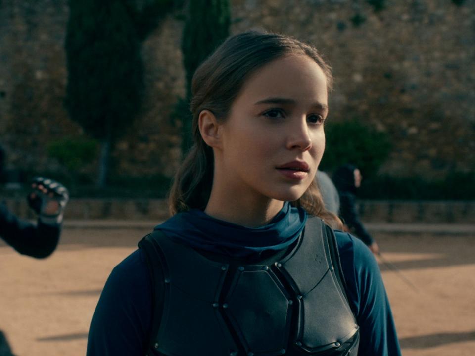 alba baptista as ava in warrior nun, a young woman wearing an armor plate on her chest standing on a fighting ground