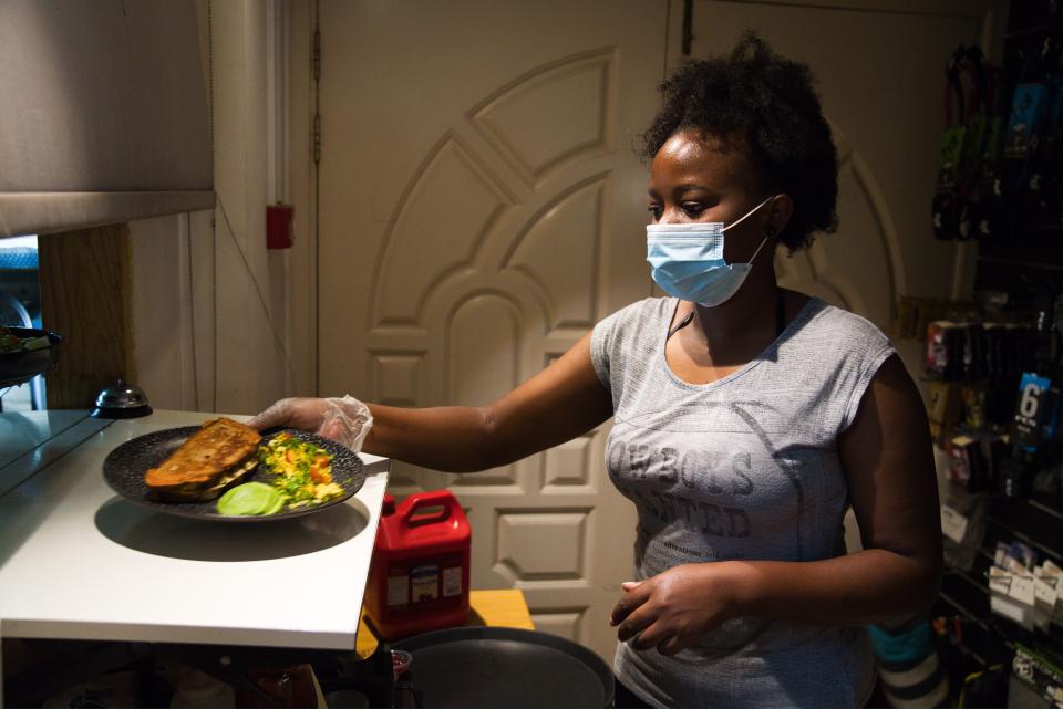 In this Thursday, May 7, 2020 photo, waitress Elizabeth Kavesu of Nairobi, Kenya, takes a plate of food for a customer at the Single Fin Cafe and Surf House while wearing a surgical mask and a glove due to the coronavirus pandemic in Dubai, United Arab Emirates. Dubai built a city on the promise of globalization, creating itself as a vital hub for the free movement of trade, people and money worldwide. Now, with events cancelled, flights grounded and investment halted, this sheikhdom in the UAE faces both the threat of the virus and a growing economic crisis. (AP Photo/Jon Gambrell)