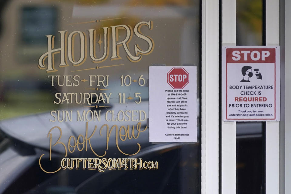 FILE - In this Nov. 15, 2020, file photo, signs on the door of Cutter's Barbershop address COVID-19 pandemic precautions, including temperature checks and sanitizing, in downtown Olympia, Wash. States in the U.S. are renewing their push for more federal money to deal with the fallout from the coronavirus outbreak and to help them distribute a vaccine when one becomes widely available sometime in 2021. (AP Photo/Ted S. Warren, File)