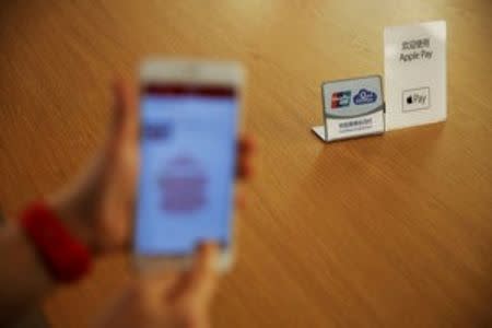 An employee uses the Apple iPhone to demonstrate to reporters how to pay using the Apple Pay service at an Apple store in Beijing, China, February 17, 2016. REUTERS/Damir Sagolj/File Photo