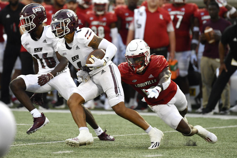 Eastern Kentucky wide receiver Matt Wilcox Jr., center, runs from the grasp of Louisville defensive back Qwynnterrio Cole, right, during the first half of an NCAA college football game in Louisville, Ky., Saturday, Sept. 11, 2021. (AP Photo/Timothy D. Easley)