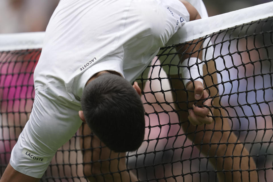 Serbia's Novak Djokovic grabs the net to stop himself toppling over as he plays Argentina's Pedro Cachin in a first round men's singles match on day one of the Wimbledon tennis championships in London, Monday, July 3, 2023. (AP Photo/Kin Cheung)