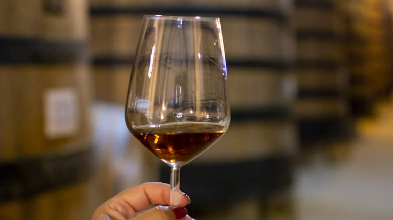 Hand holding Marsala wine in front of wooden casks