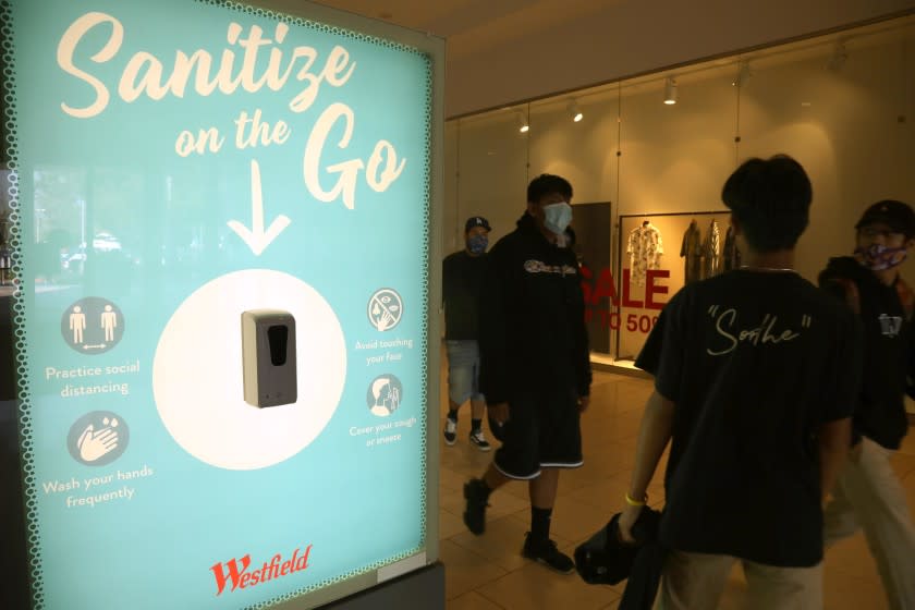 ARCADIA, CA - OCTOBER 07, 2020 - Shoppers walk past a "Sanitize on the Go," station to keep shoppers safe from coronavirus at the Westfield Santa Anita shopping mall in Arcadia on October 7, 2020. This is the first day customers return to indoor shopping after Los Angeles County eases restrictions and have reopened the malls and the individual stores. Such stores have been closed for weeks, but reopened Wednesday at 25% capacity. Westfield Santa Anita has placed Covid-related signage with one-way traffic, 6 feet distancing when waiting to get into individual stores, hand sanitizing stations and mask are required before entering the mall. (Genaro Molina / Los Angeles Times)
