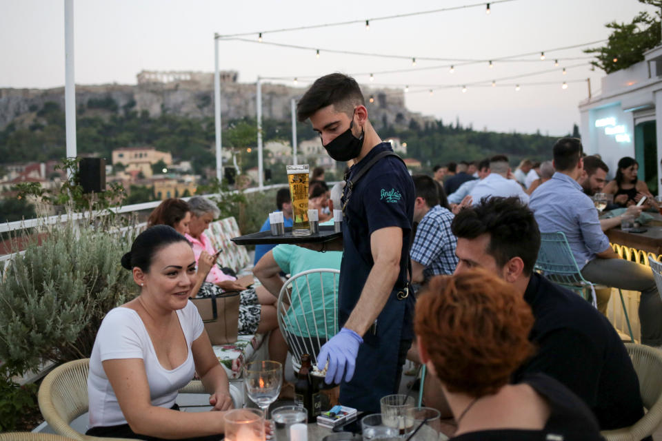 A waiter serves patrons at a bar in Athens, Greece, Aug. 1. Since the country began lifting lockdown restrictions, the number of coronavirus cases has spiked. (Photo: Costas Baltas / reuters)