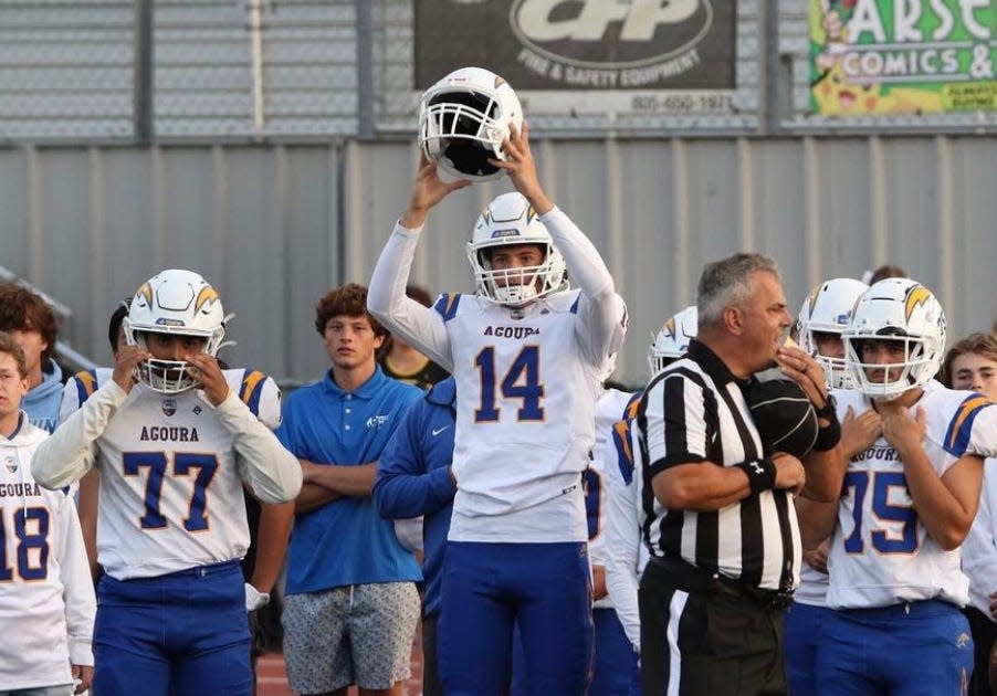 Agoura High quarterback Ty Dieffebach holds up the football helmet of Agoura High freshman Carter Stone before Friday night's game at Ventura High. Stone, a 15-year-old freshman lineman, died last week after complications from shoulder surgery.