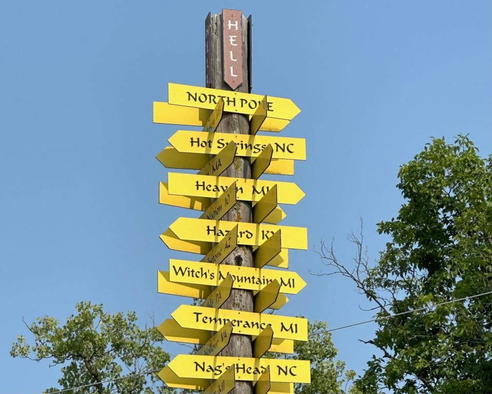 Wooden post covered with yellow arrows of town names including Hot Springs, NC; Heaven, MI; and Witch's Mountain, MI 