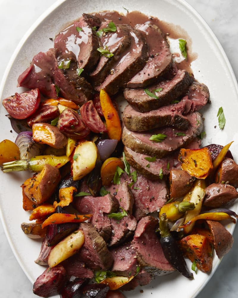 An overhead view close up of sliced chateaubriand on a platter with roasted root vegetables.