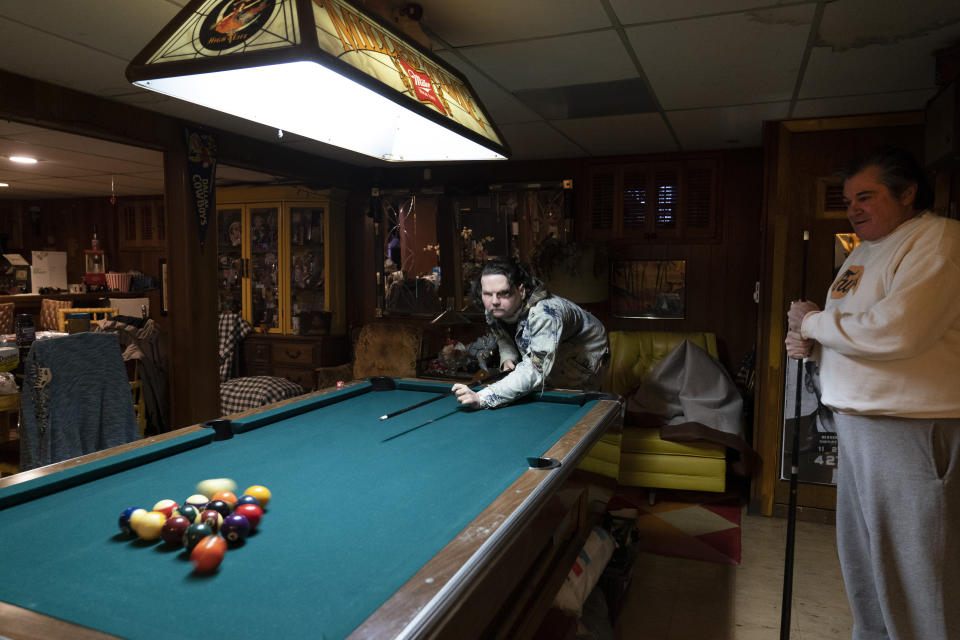 Joe DiMeo plays pool with his father John at their home, Thursday, Jan. 28, 2021, in Clark, N.J., six months after an extremely rare double hand and face transplant. Back in 2018, DiMeo fell asleep at the wheel, he said, losing control of his car, which hit a curb and utility pole, flipped over, and burst into flames. (AP Photo/Mark Lennihan)