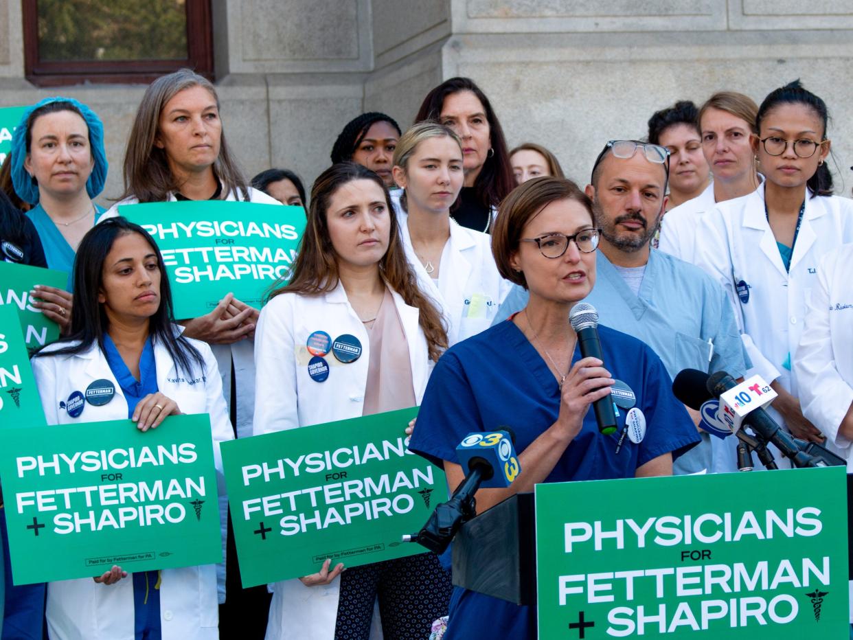 Doctor speaking at podium, with physicians in lab coats behind her