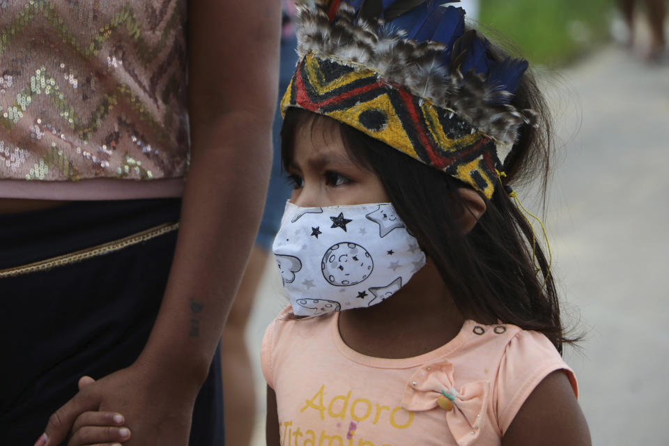 A girl wearing a mask walks holding hands with an adult after the funeral of Chief Messias Martins Moreira, 53, of the Kokama ethnic group, who died of Covid-19, at Parque das Tribos in Manaus, Amazonas state, Brazil, Thursday, May 14, 2020. (AP Photo/Edmar Barros)