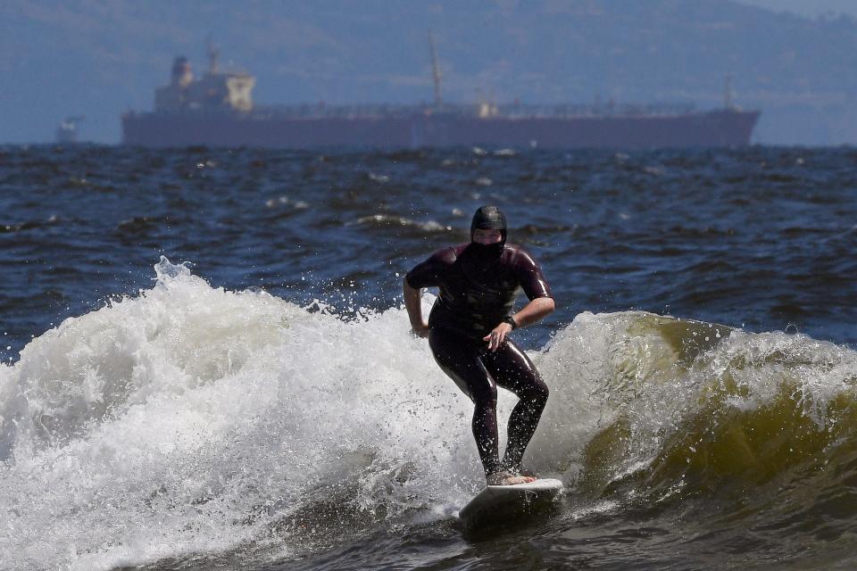 Tim O'Rourke surfs with a face covering to protect him from the coronavirus, at Venice Beach, Wednesday, May 13, 2020, in Los Angeles.