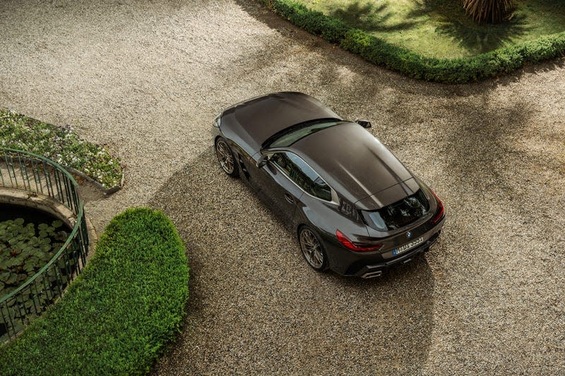 A brown BMW shooting brake concept is parked in gravel near lush plantings. You are looking down on it from above.