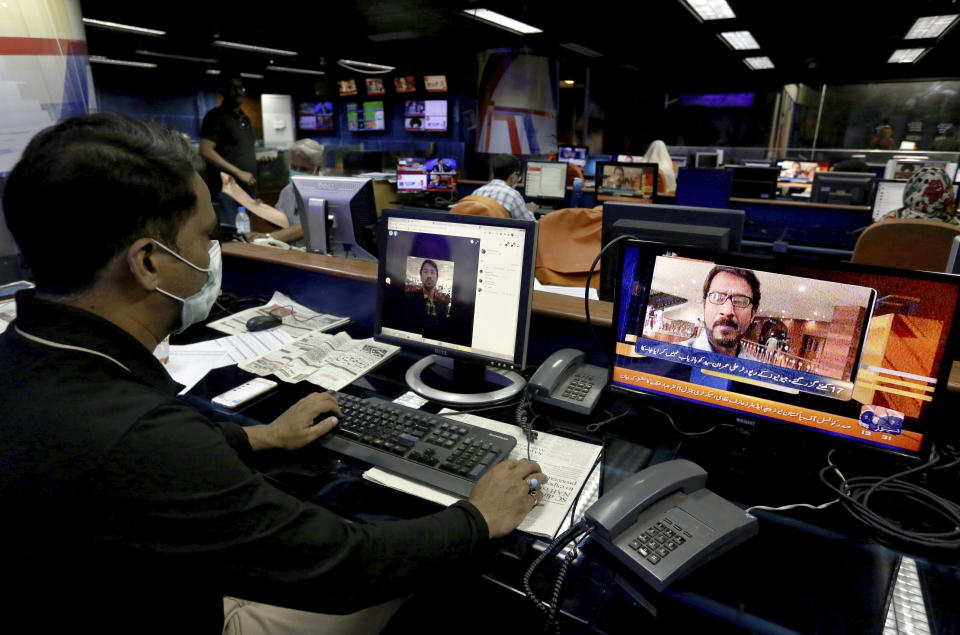 Employees of Geo News television work at their office while a television channel broadcasts news regarding one their reporter Ali Imran Syed, missing in Karachi, Pakistan, Saturday, Oct. 24, 2020. The Geo bureau chief in Karachi said Saturday that police registered the journalist’s disappearance as an “abduction” case without naming suspects. (AP Photo/Fareed Khan)