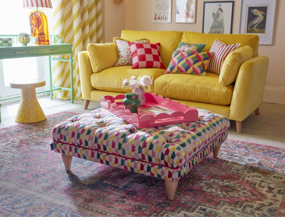 a yellow couch with a pink and white pillow and a pink coffee table