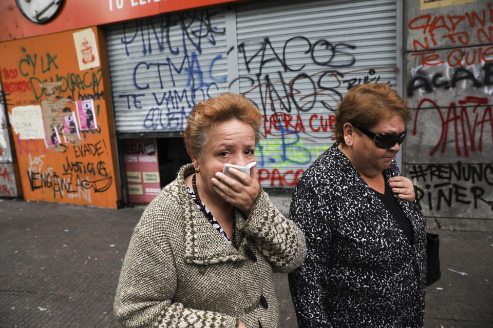 Women walk past a store the day after it was looted by anti-government protesters in Santiago, Chile, Tuesday, Oct. 29, 2019. Fresh protests and attacks on businesses erupted in Chile Monday despite President Sebastián Pinera's replacement of eight key Cabinet ministers and his attempts to assure the country he has heard calls for greater equality and improved social services. (AP Photo/Rodrigo Abd)