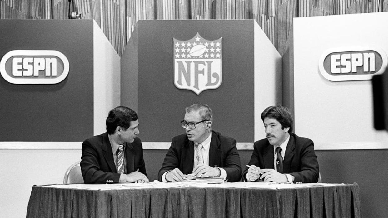 <div>NEW YORK, NY - APRIL 27: (EDITORS NOTE: Image has been shot in black and white. Color version not available.) ESPN host George Grande (left) talks to analysts Paul Zimmerman (center) of Sports Illustrated and Howard Balzer of The Sporting News during a broadcast of the National Football League player draft at the Sheraton Hotel on April 27, 1982 in New York, New York. (Photo by George Gojkovich/Getty Images)</div>