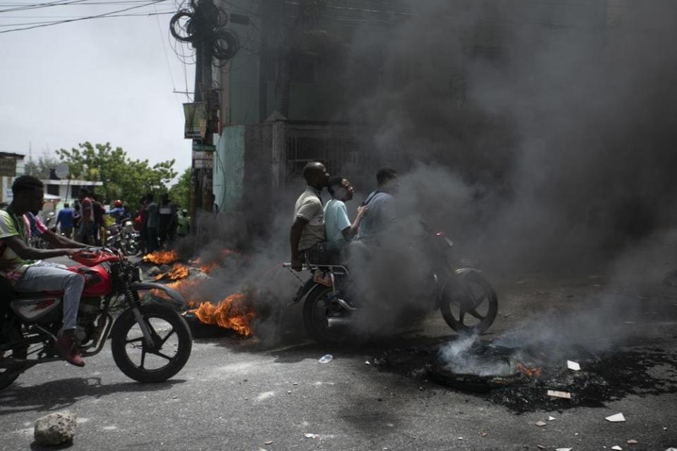 A motorcycle taxi driver carries clients past a burning barricade set by taxi drivers to protest the country’s fuel shortage in Port-au-Prince, Haiti, Wednesday, July 13, 2022. (AP Photo/Odelyn Joseph)