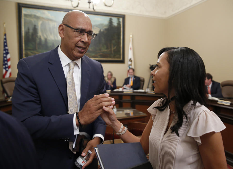 FILE - Democratic Assembly members Chris Holden, of Pasadena, left, and Autumn Burke, of Marina del Rey, shake hands after the wildfire bill they co-authored, with Assemblyman Chad Mayes, R-Yucca Valley, was approved by Senate committee in Sacramento, Calif., Monday, July 8, 2019. A California lawmaker introduced a bill Thursday, Jan. 19, 2023, that would require schools that play major college sports to pay some athletes as much as $25,000 annually, along with covering the cost of six-year guaranteed athletic scholarships and post-college medical expenses. The College Athlete Protection Act is sponsored by Assembly member Chris Holden. (AP Photo/Rich Pedroncelli, File)