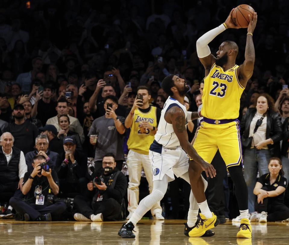 Lakers forward LeBron James holds the ball away from Mavericks guard Kyrie Irving while looking around the court