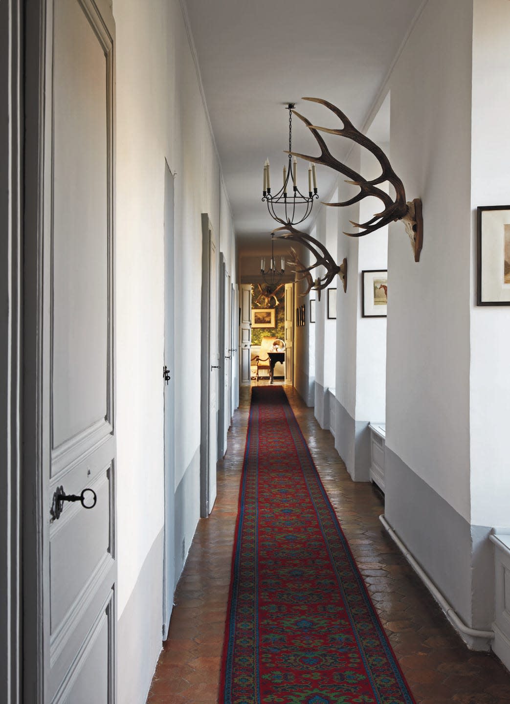 hallway with white walls and red patterned runner and stag horns mounted along the right wall