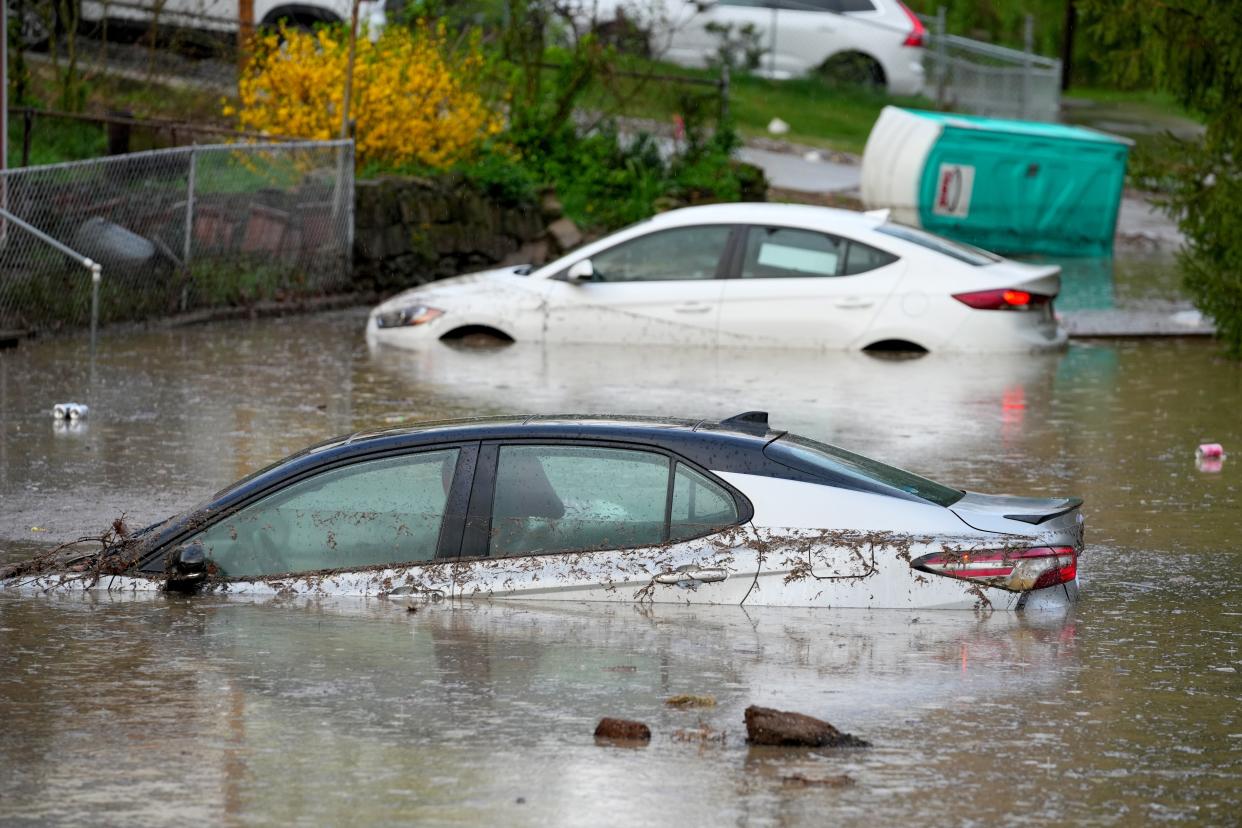 Residents observe cars flooded in a low-lying parking lot and grassy area, Tuesday, April 2, 2024, near the intersection of Delta Avenue and Columbia Parkway in the Columbia Tusculum neighborhood in Cincinnati. Several homes that sit at the base of a hill near the intersection have flooded, neighbors said.