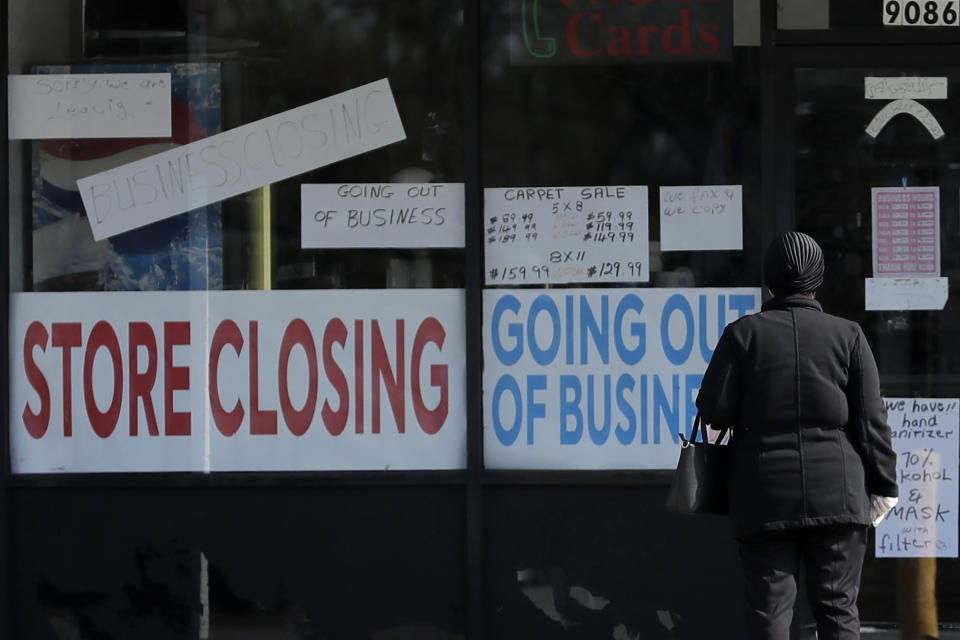 A woman looks at signs at a store closed due to COVID-19 in Niles, Ill., Wednesday, May 13, 2020. (AP Photo/Nam Y. Huh)