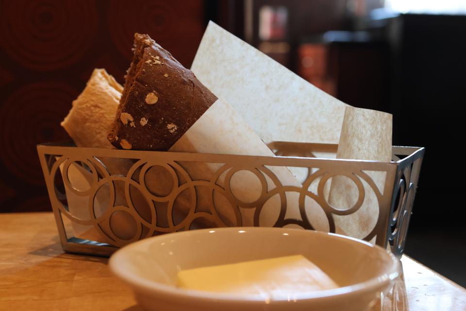 A metal bread basket on a table at The Cheesecake Factory.