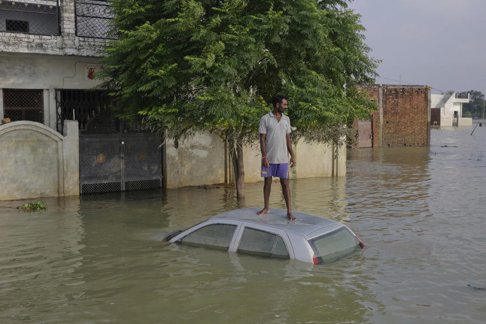 An Indian man, stands on his car that got submerged in flood