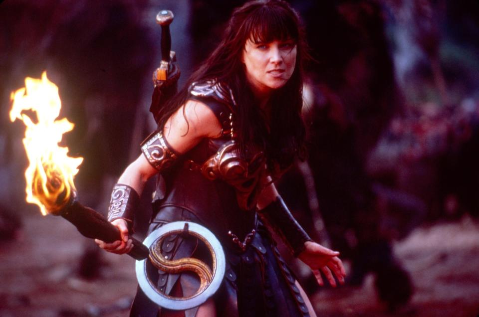 Lucy Lawless dressed as Xena holding a flaming torch and chakram in a scene from "Xena: Warrior Princess."