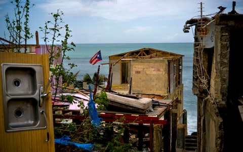 A Puerto Rican national flag is mounted on debris of a damaged home in the aftermath of Hurricane Maria - Credit: AP